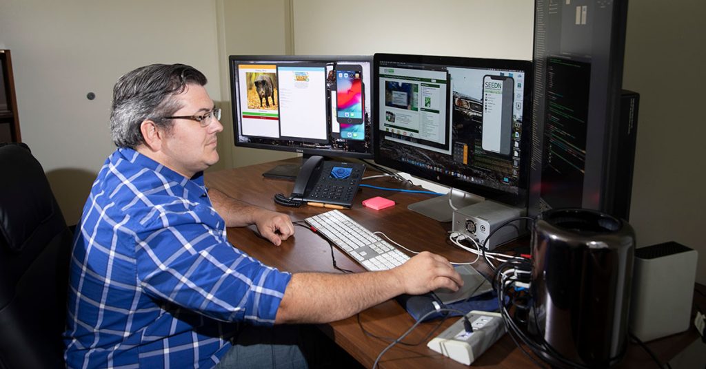 Person seated at desk with computer screens working on app development.