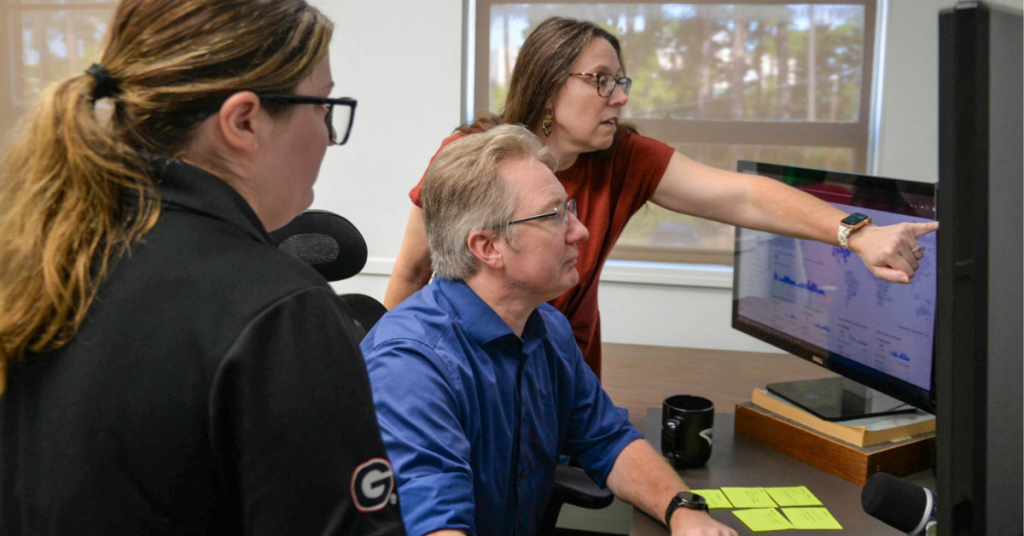 Three team members review a data dashboard, with one person pointing to information on the screen.