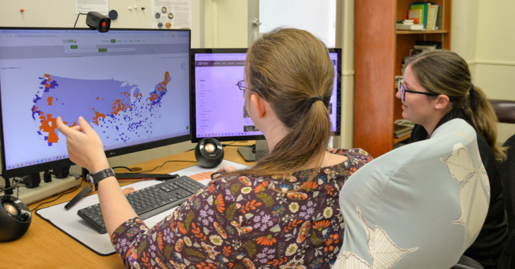 Two team members review an invasive species distribution map on a computer screen.
