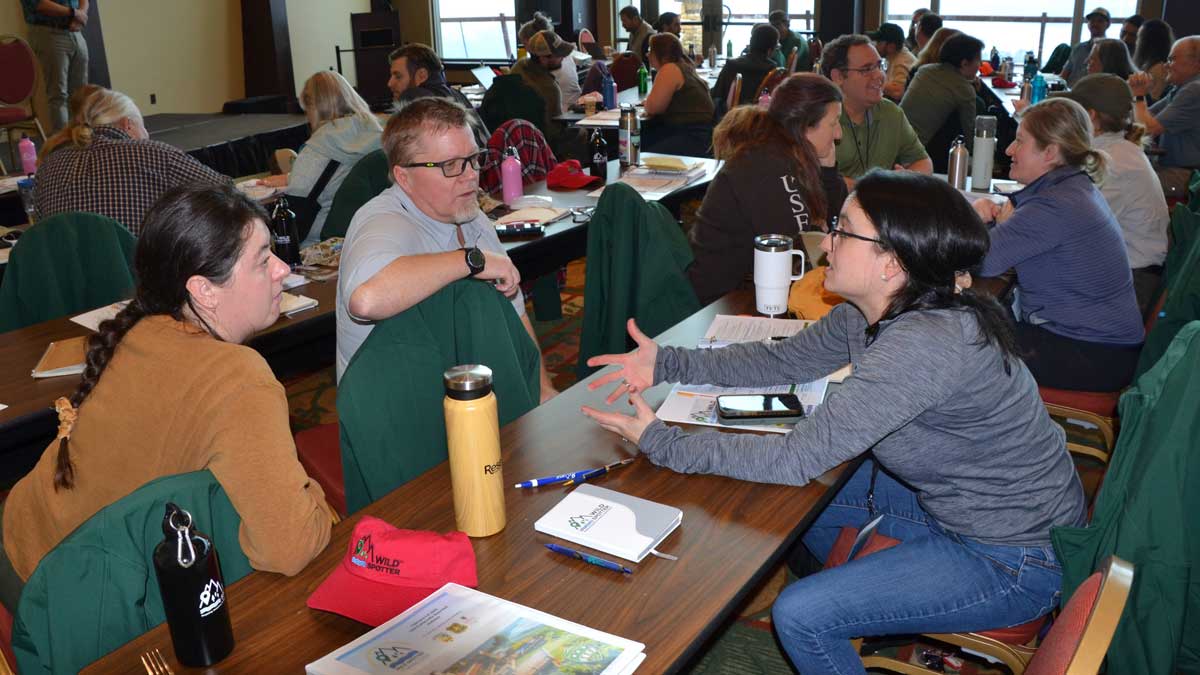 Ambassador Training participants collaborate around a table with laptops, notes, and planning sheets.