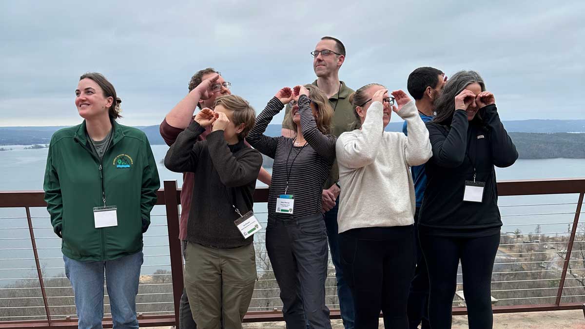 Ambassador Training participants pose on an overlook, with several making binoculars with their hands.