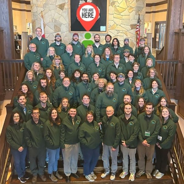 Invasive Species Ambassador graduates wearing green jackets pose together on a staircase.
